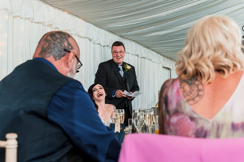 Man giving wedding speech, others laughing and listening.