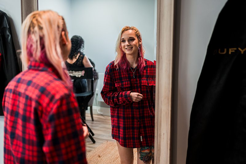 Woman in red checkered shirt smiling at mirror.