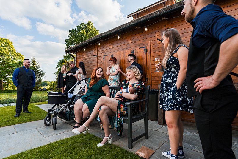 Outdoor gathering with people socialising near wooden cabin.
