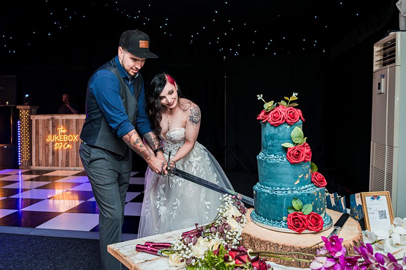 Couple cutting wedding cake with a sword.