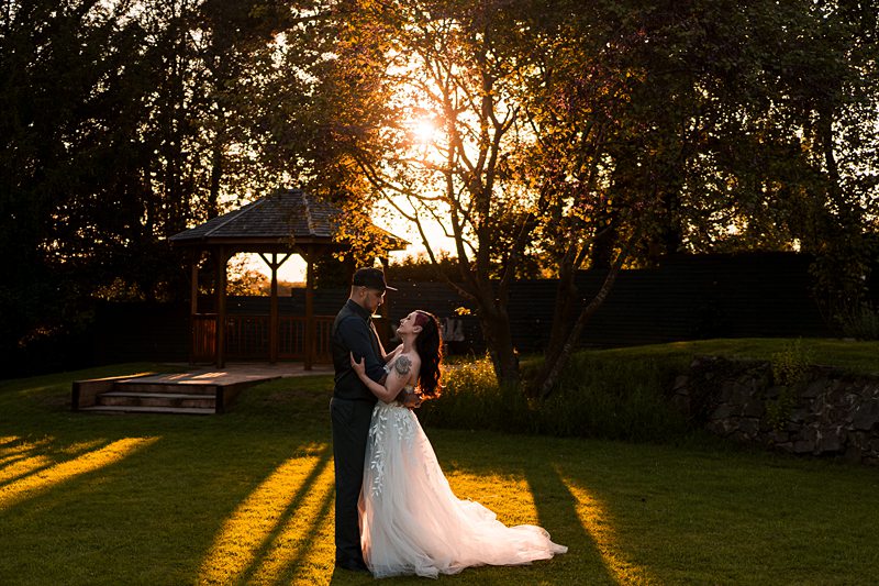 Bride and groom embracing at sunset in a garden.
