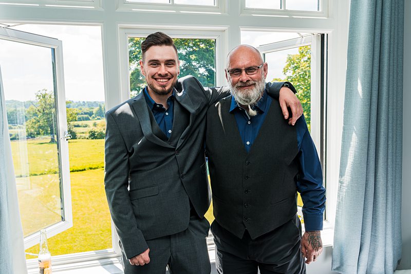 Two men in suits smiling near a window.