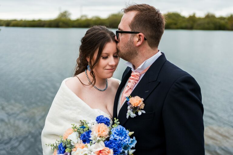 Bride and groom by the lake, wedding flowers present.