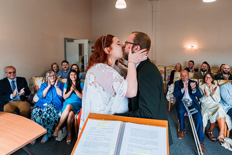 Couple kissing at ceremony with guests clapping.