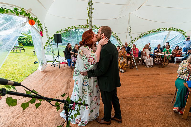 Couple kissing during wedding ceremony in decorated tent.