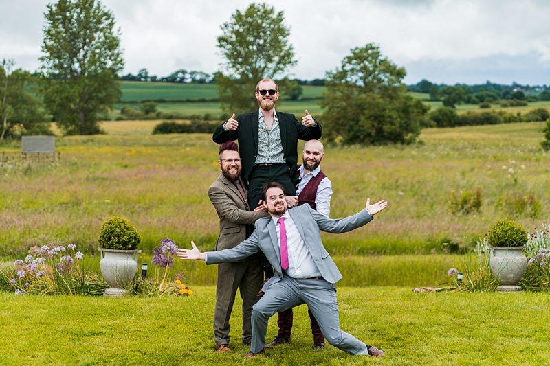 Four men smiling in a countryside field.