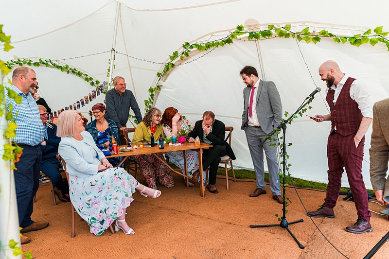 Group of people giving speeches in a garden tent.