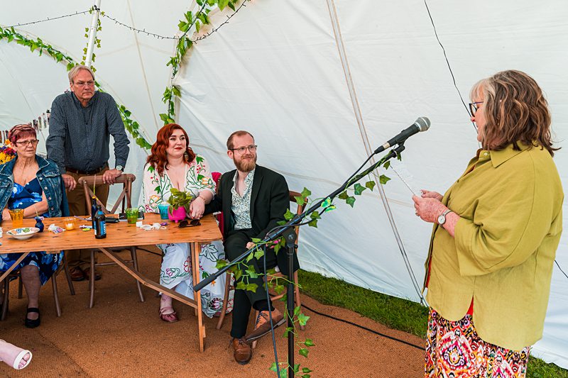 Woman giving a speech to seated guests in tent.