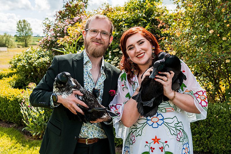 Couple holding ducks in a garden.
