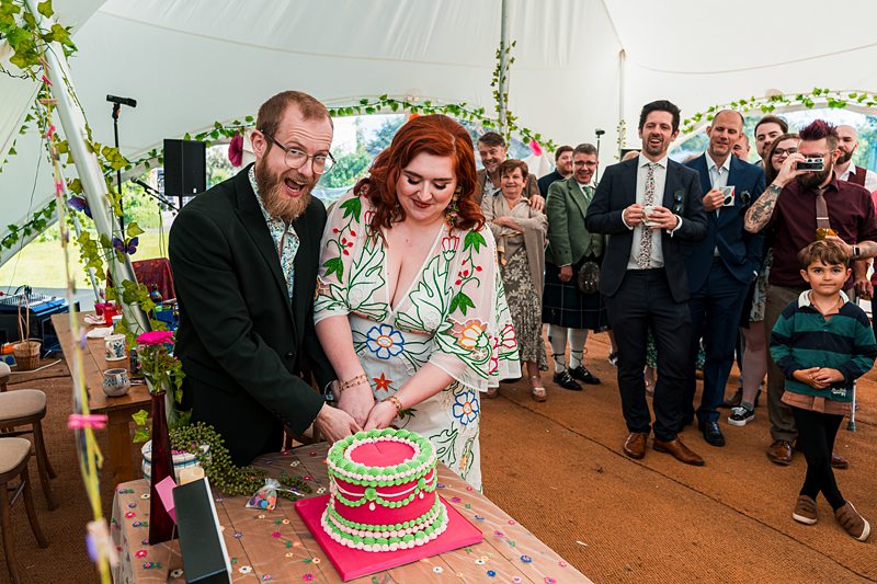 Couple cutting wedding cake with guests watching.