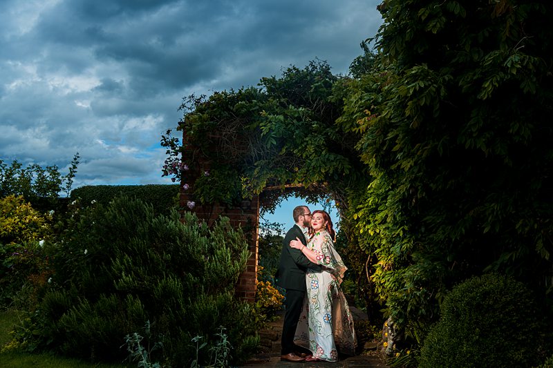 Couple embraces under garden archway.