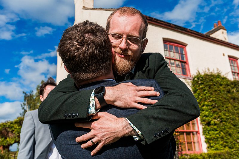 Two men hugging outdoors at a wedding.