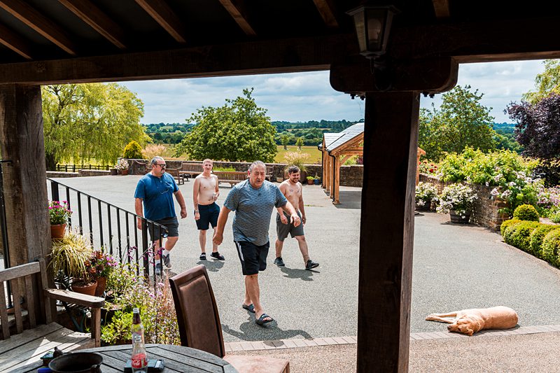 Group of men walking outdoors with garden view.