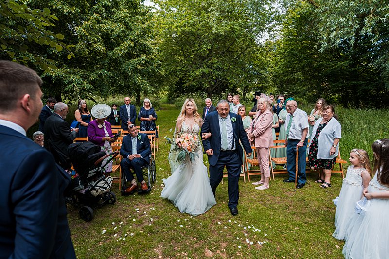 Bride walking down outdoor aisle with guests.