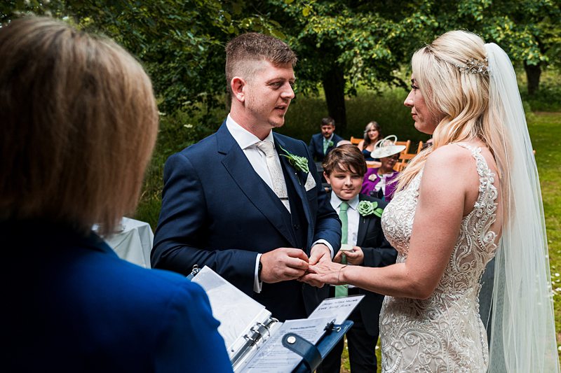 Bride and groom exchange rings during outdoor ceremony.