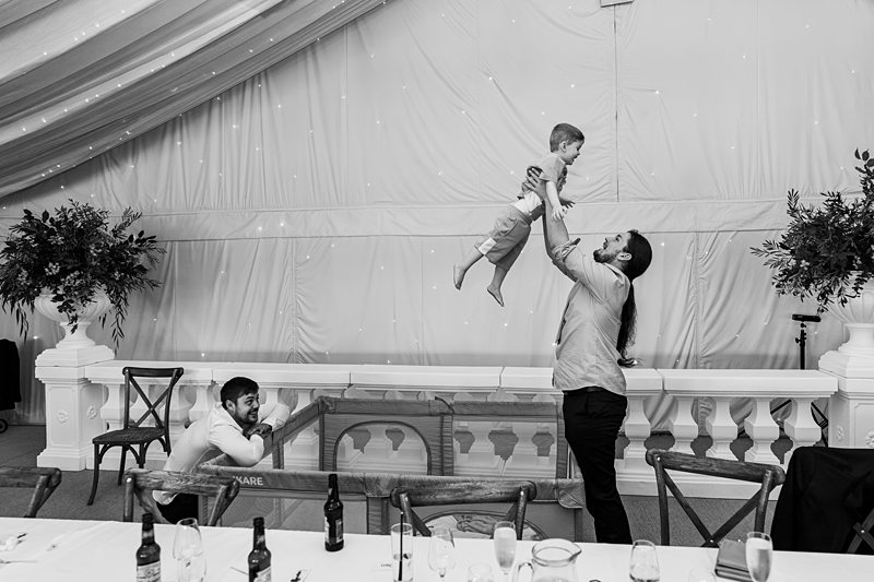 Man lifts child at event, another watches, monochrome.