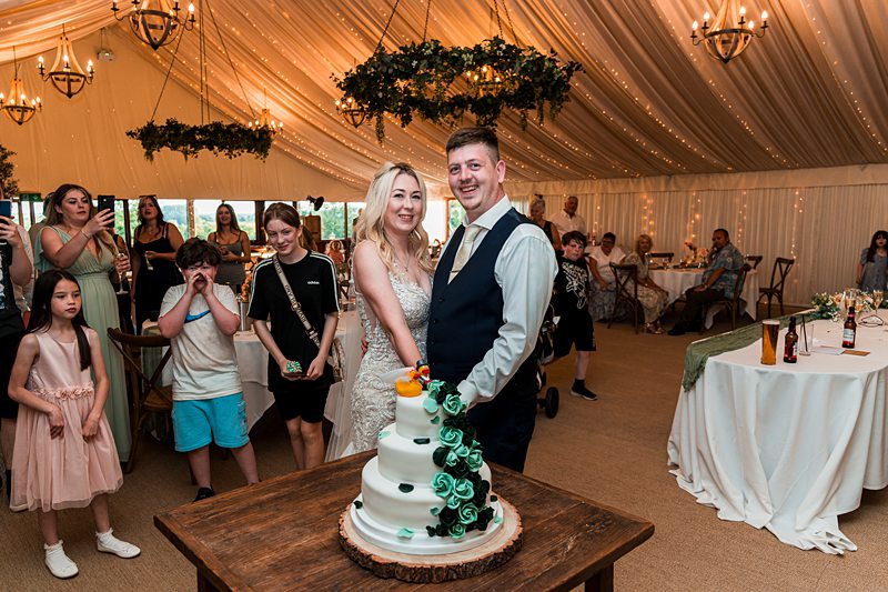 Couple cutting wedding cake in decorated marquee.