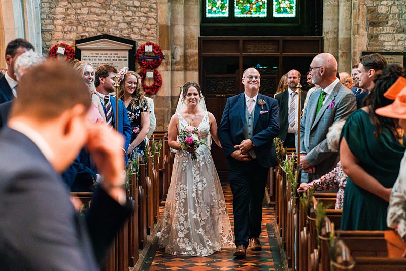 Bride walking down church aisle with father.