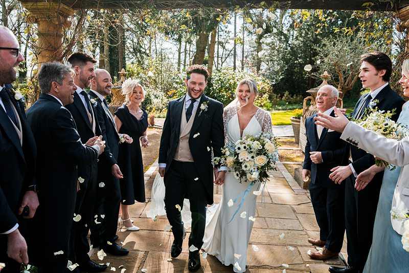 Wedding couple walking amid joyful guests outdoors.