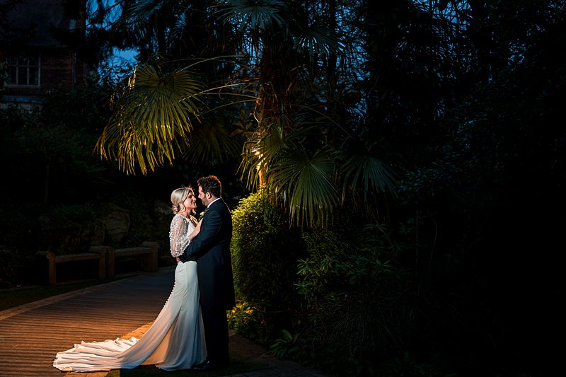 Couple embracing outdoors at night under palm trees.