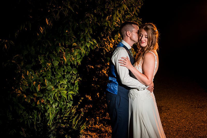 Couple embracing in evening light by greenery.