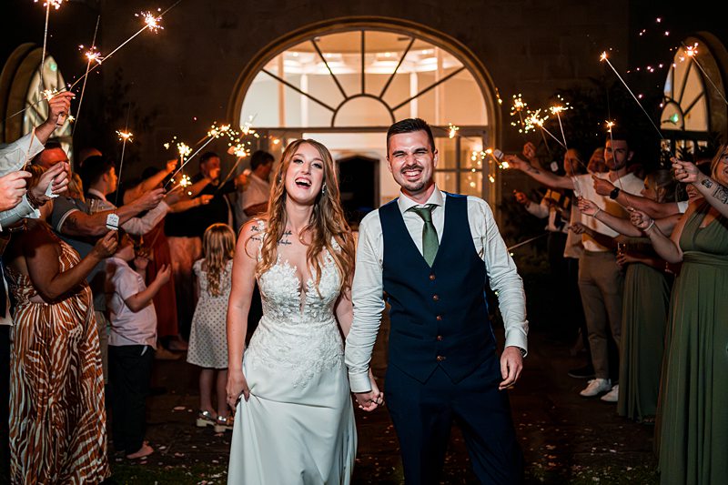 Happy newlyweds hold sparklers at wedding reception.