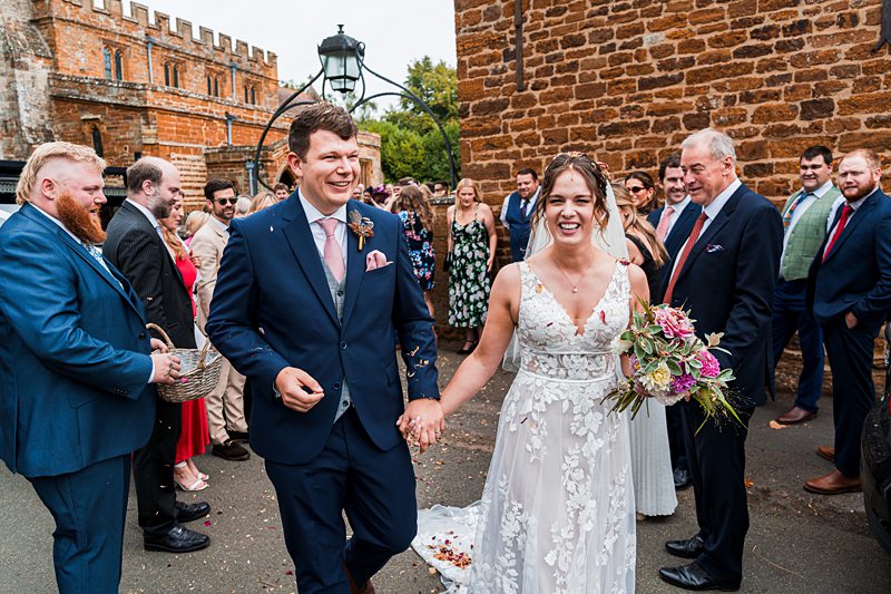 Just married couple walking, smiling with guests nearby.