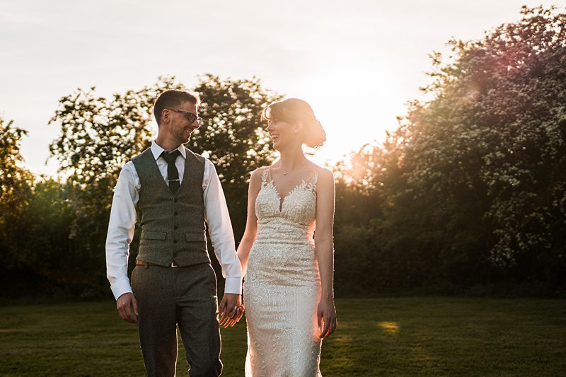 Couple smiling at sunset in wedding attire.