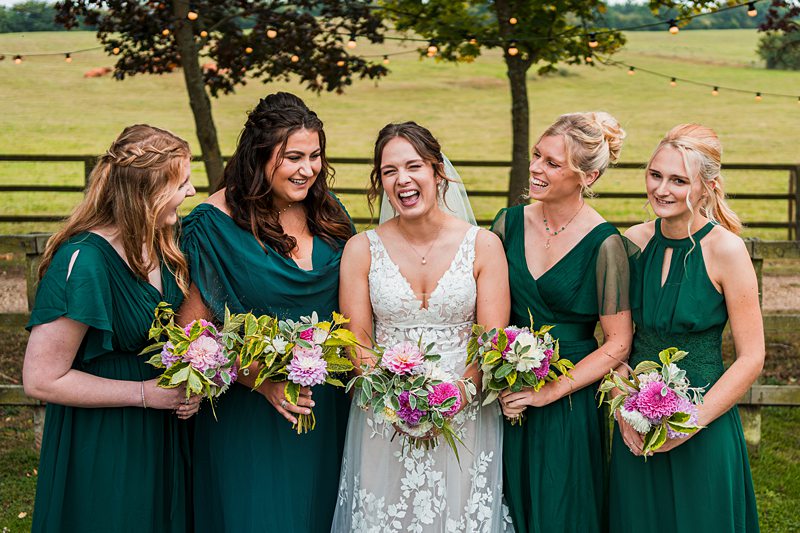 Bride with bridesmaids in green dresses laughing outdoors.