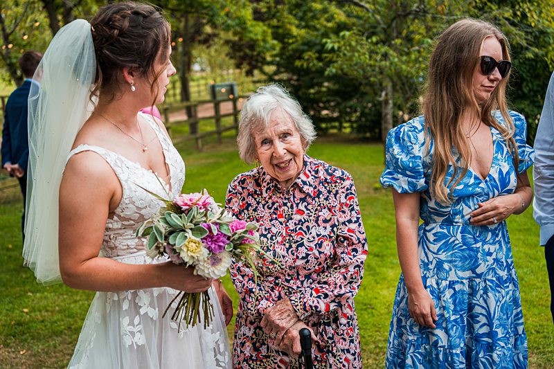 Bride with bouquet, elderly woman, and young woman outdoors.