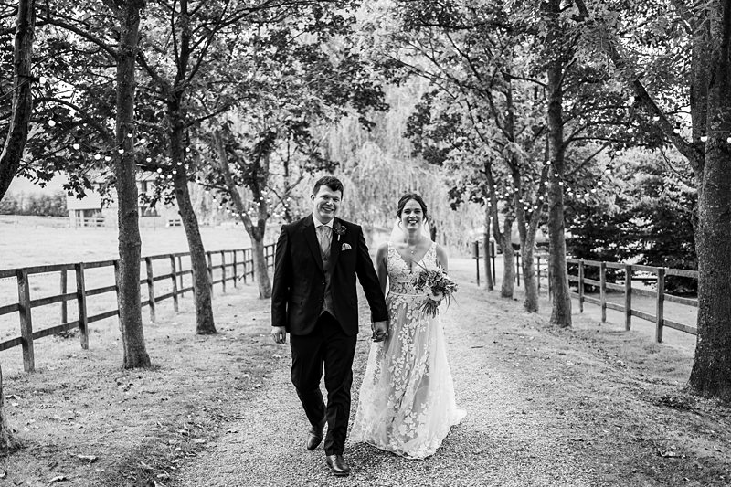 Bride and groom walking on leafy pathway.