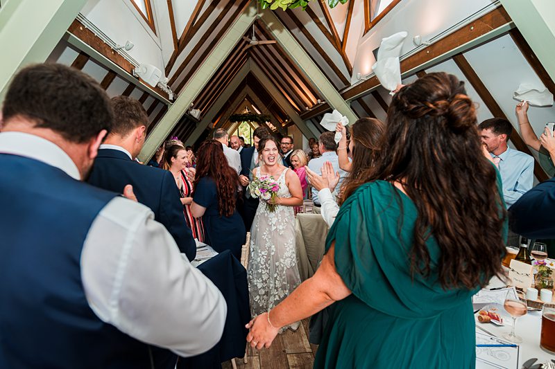 Bride enters reception, guests cheer with napkins.