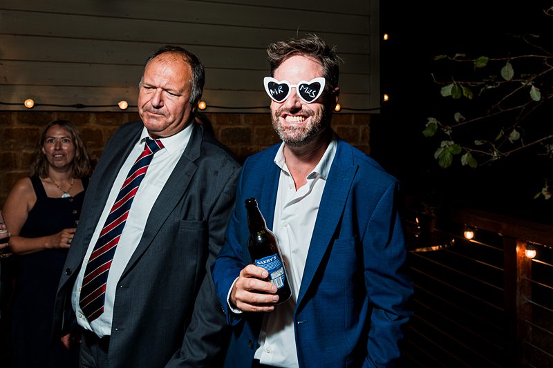 Man in heart sunglasses holds beer at party.