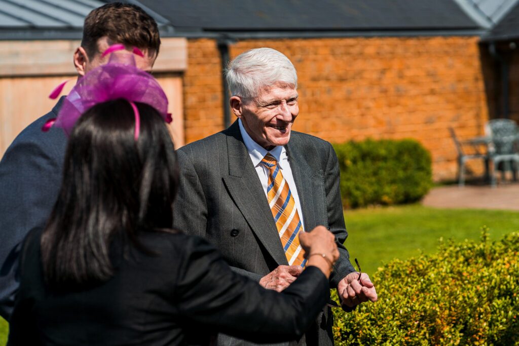 Smiling elderly man in garden setting with friends.