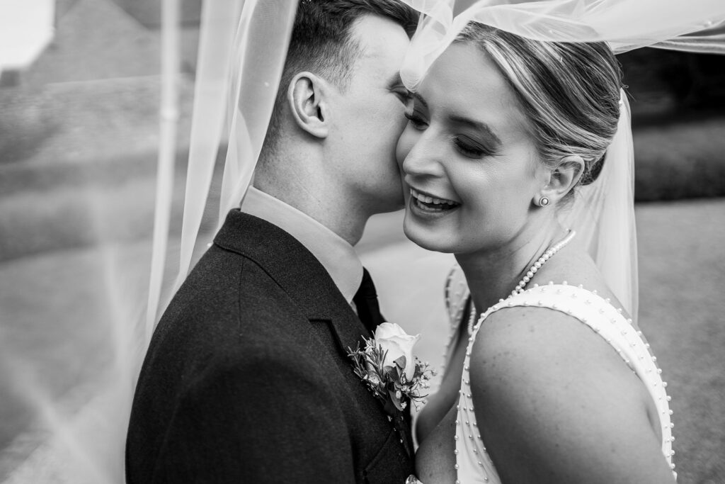 Bride and groom embracing under veil, smiling happily.