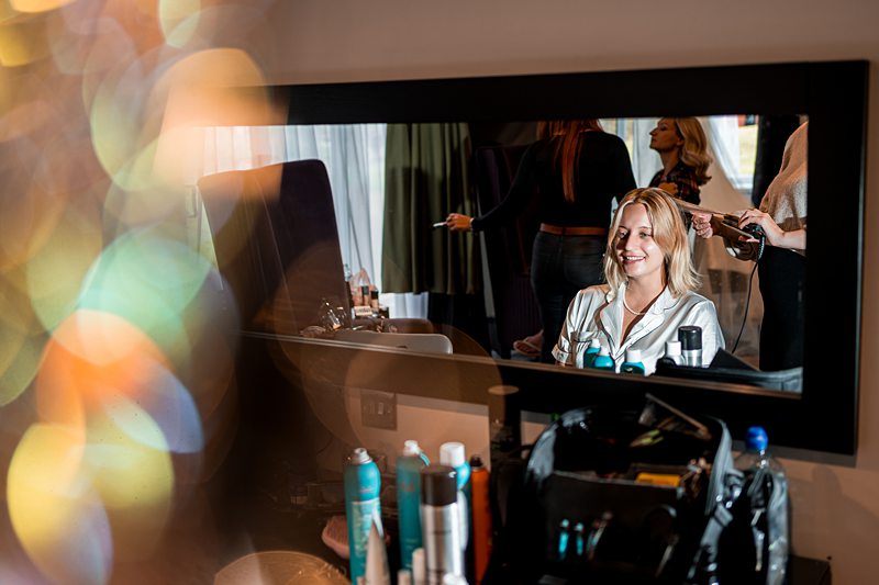 Woman smiling during hair styling in mirror reflection.