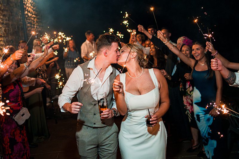 Wedding couple kissing surrounded by guests with sparklers.