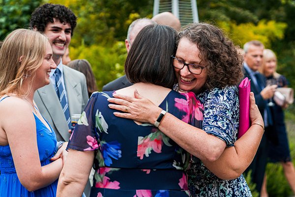 People hugging at outdoor gathering, smiling.