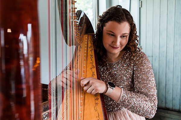 Woman playing harp in sequined blouse.