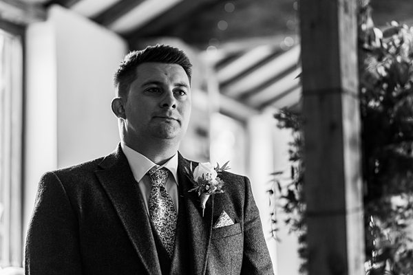 Man in suit at rustic wedding venue.
