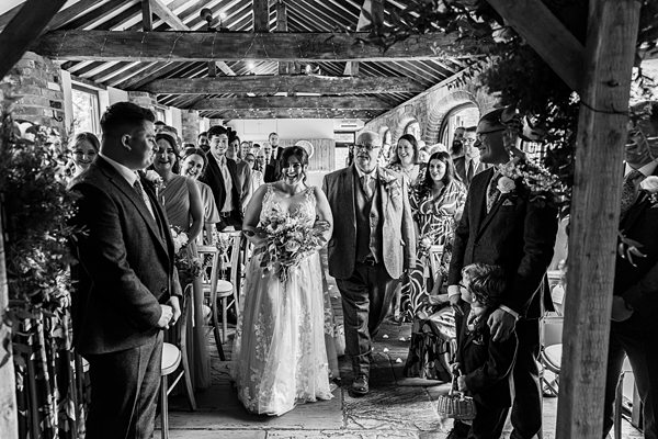 Bride walking down aisle at indoor wedding ceremony.