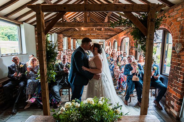 Wedding couple kissing during rustic ceremony with guests.