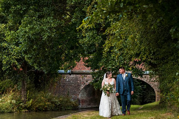Couple walking by canal under a brick bridge.