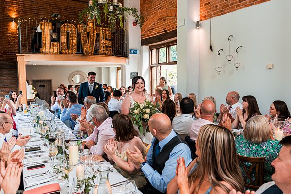 Bride entering reception, guests applauding at wedding venue.
