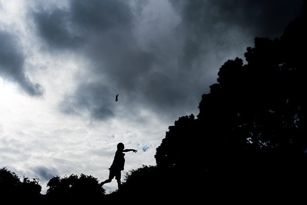 Silhouette of child playing under cloudy sky.
