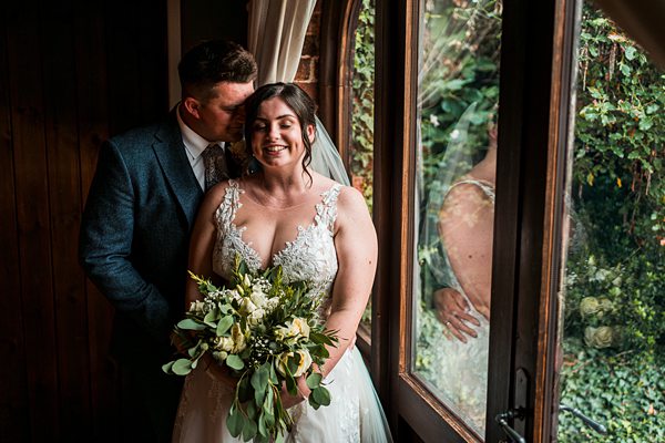 Bride and groom embracing by a window.