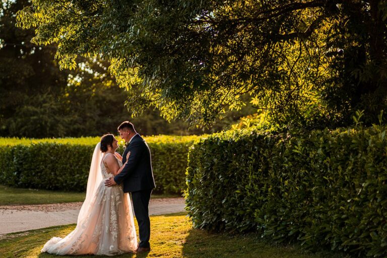 Couple embracing in sunlit garden setting.