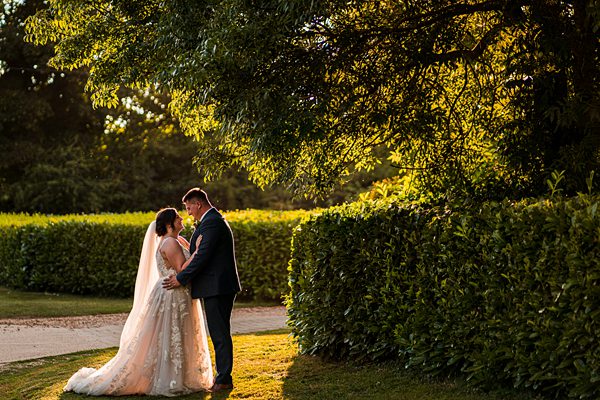 Bride and groom embrace in scenic garden.