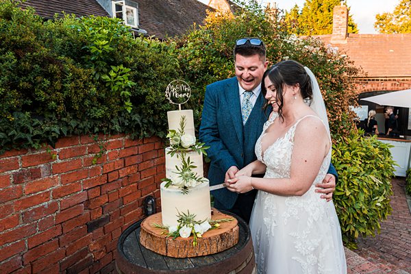 Couple cutting rustic wedding cake outdoors.