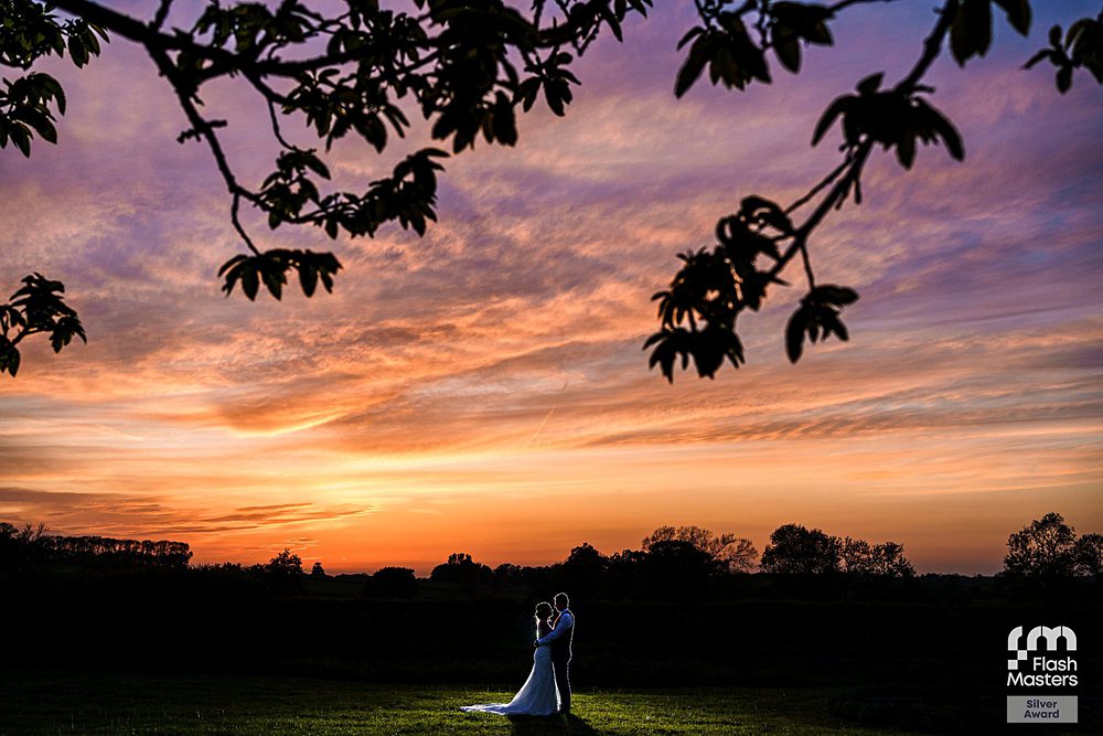 Bride and groom at sunset under tree branches.